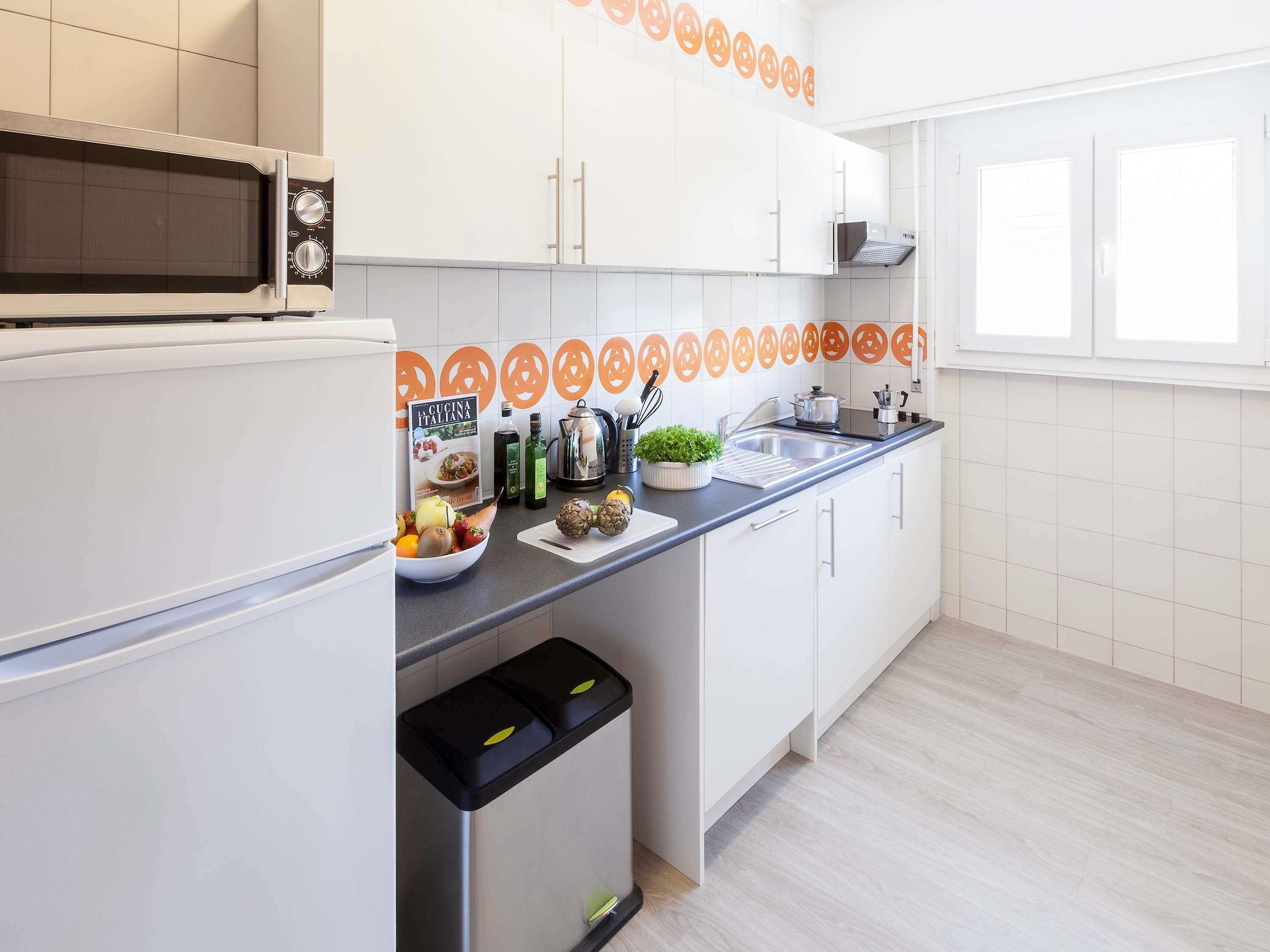 A modern kitchen with white cabinets, a microwave, a sink, and a window.