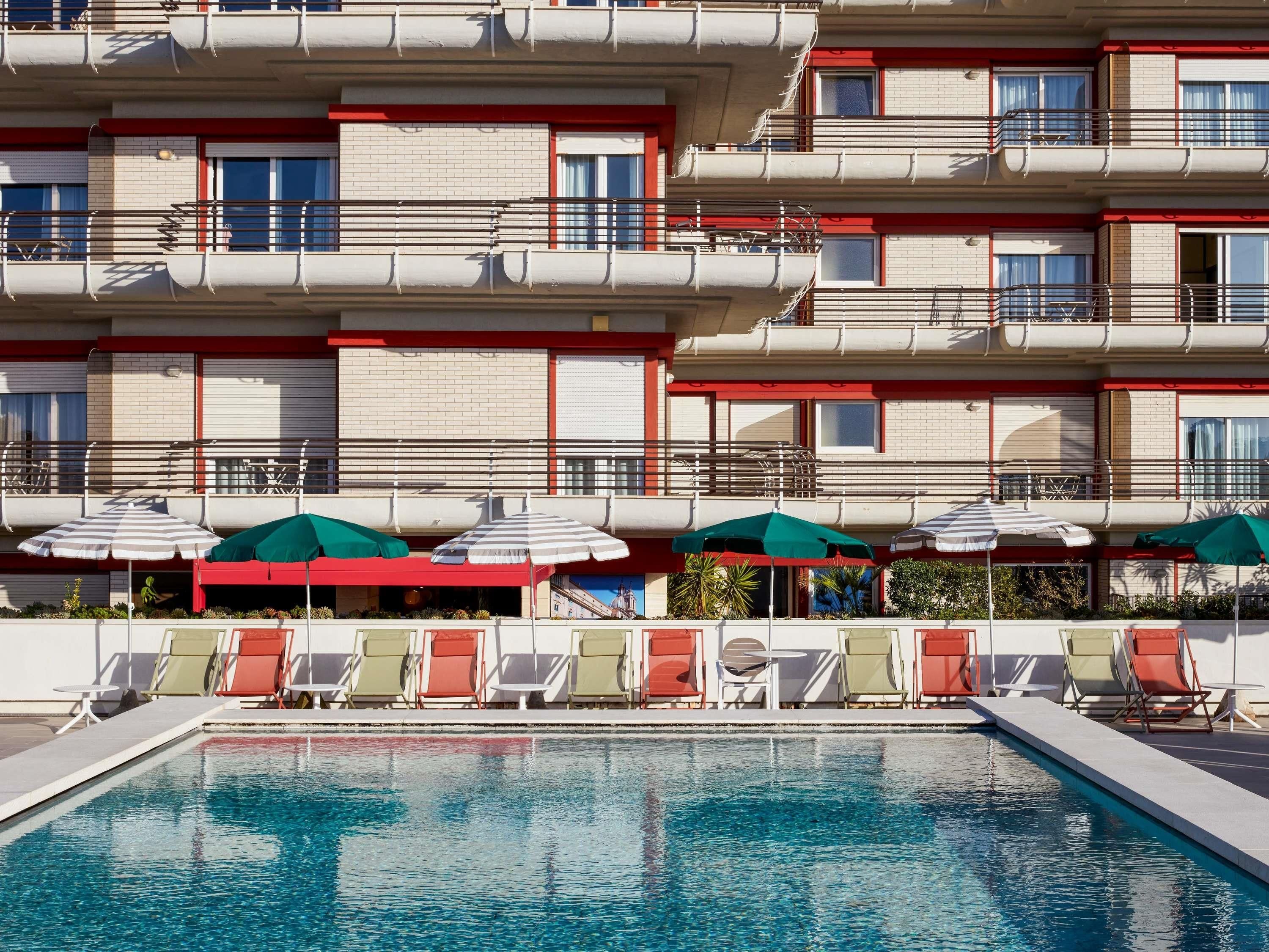 Ein Hotel mit Poolbereich, mehreren Balkonen und Außenbereich mit Sonnenschirmen.