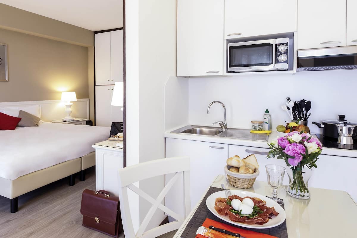 Une chambre d’hôtel équipée d’un lit, d’une table de chevet, d’une lampe et d’une kitchenette comprenant un four à micro-ondes, un évier et une cuisinière.