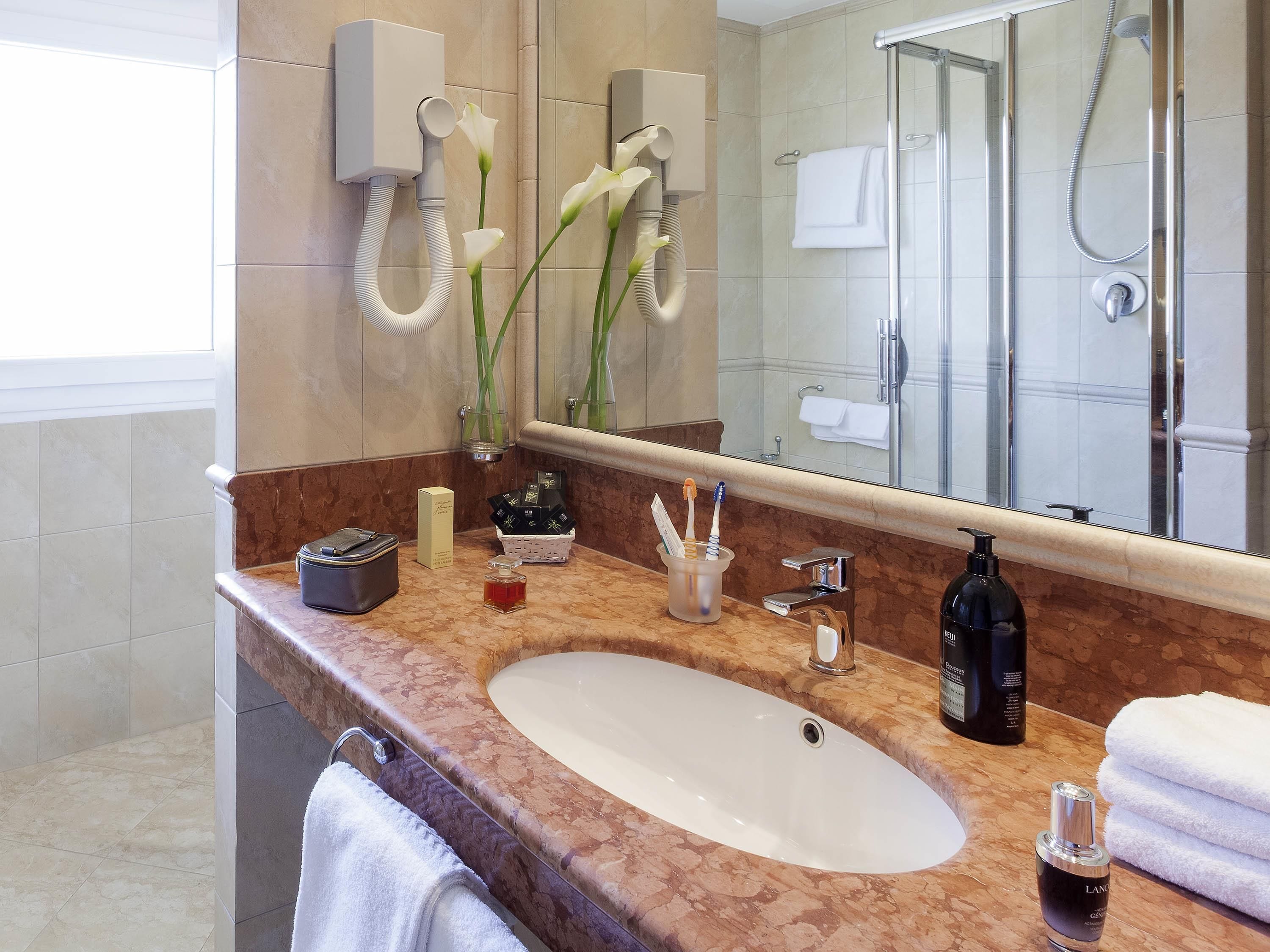 Een badkamer met een marmeren wastafel, een douchecabine van glas, een handdoekhouder en een spiegel die het douchegedeelte weerspiegelt.