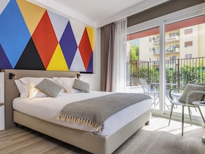 A hotel room with a large bed, a balcony with outdoor seating, and a colorful geometric wall design.