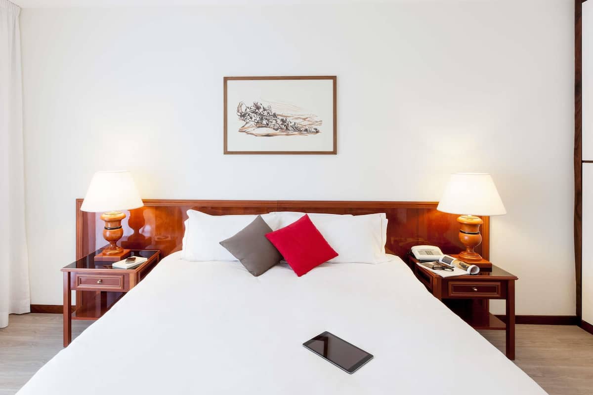 Une chambre d’hôtel avec un grand lit, deux tables de chevet avec des lampes, un tableau encadré au mur et un téléphone sur la table de chevet.
