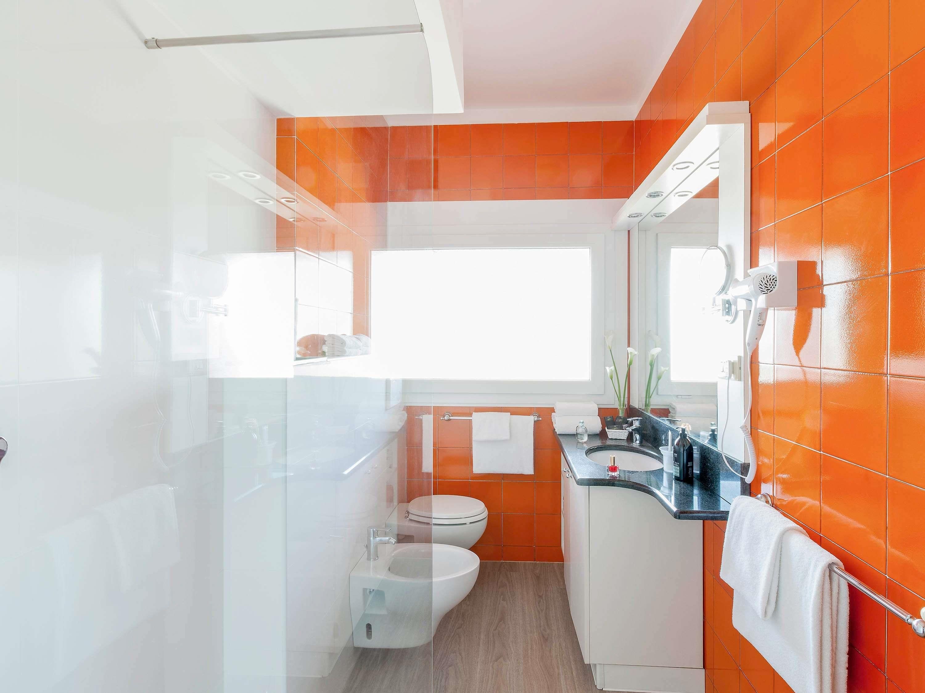 A modern bathroom with a glass shower enclosure, a white toilet, and an orange-tiled wall.