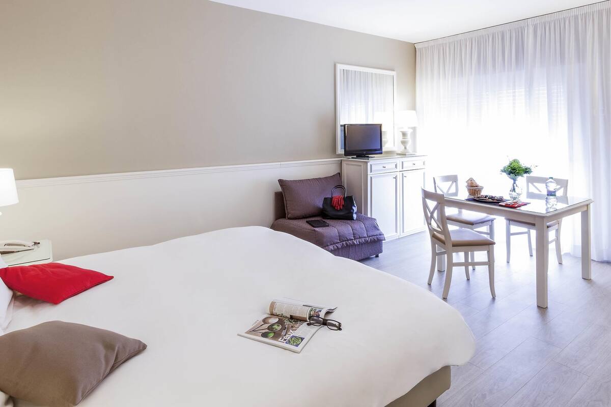 Une chambre d’hôtel équipée d’un lit, d’un bureau, d’une chaise, d’une télévision et d’une fenêtre avec des rideaux.