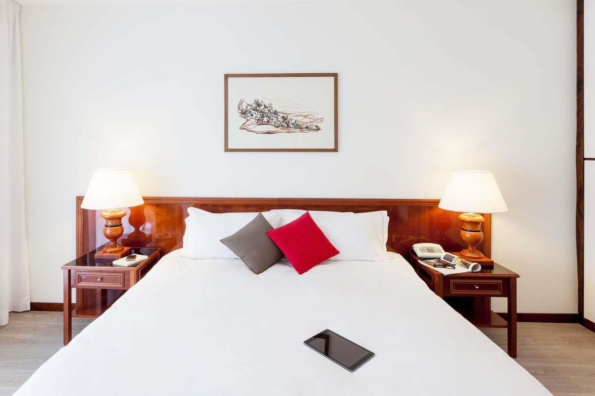 A hotel room with a large bed, two bedside tables with lamps, a framed picture on the wall, and a bedside phone.