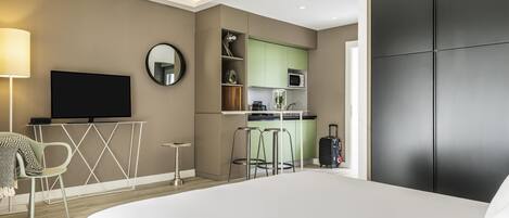 Una habitación de hotel moderna con una cama, un televisor, una pequeña cocina y una maleta.