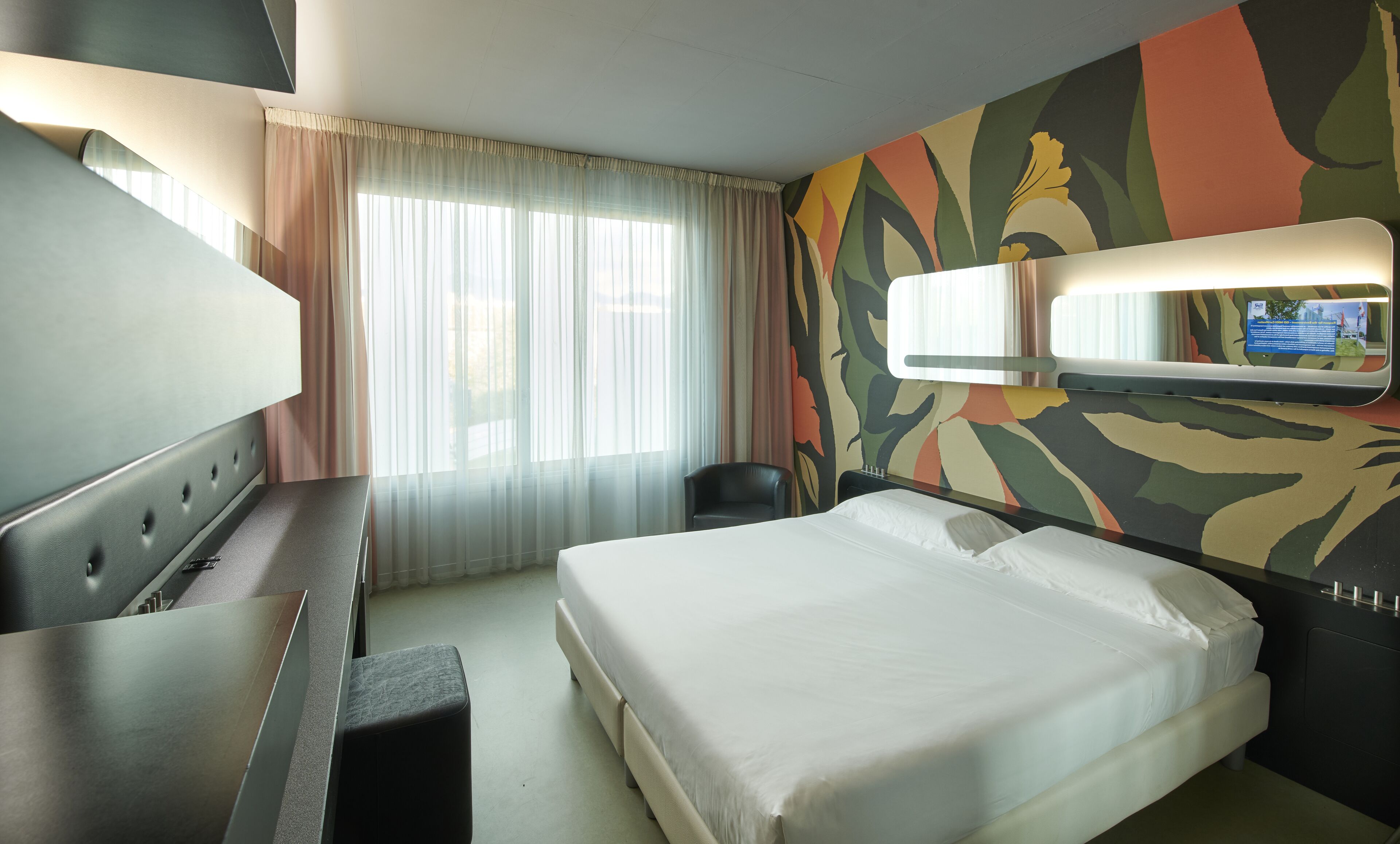 Een hotelkamer met een bed, een bureau, een stoel, een televisie en een raam met gordijnen.