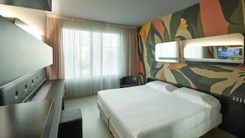 Een hotelkamer met een bed, een bureau, een stoel, een televisie en een raam met gordijnen.