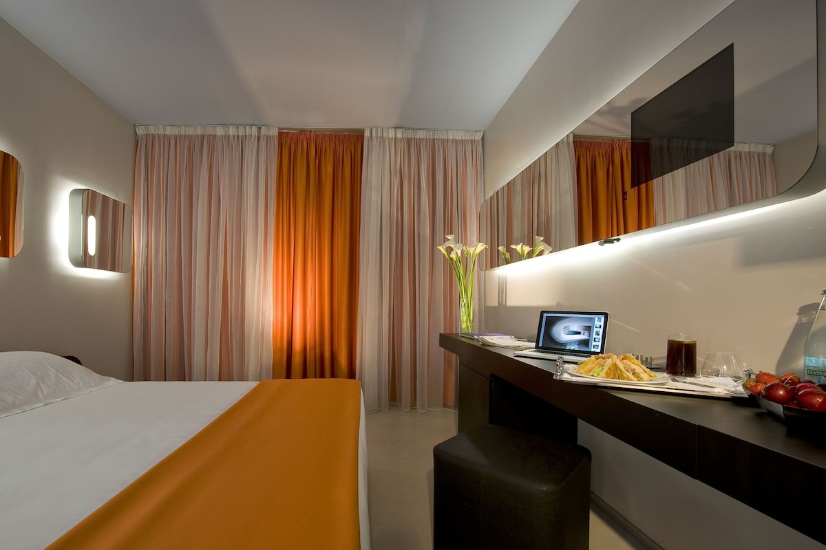 Una habitación de hotel con una cama, un escritorio con una computadora portátil, un espejo y cortinas.