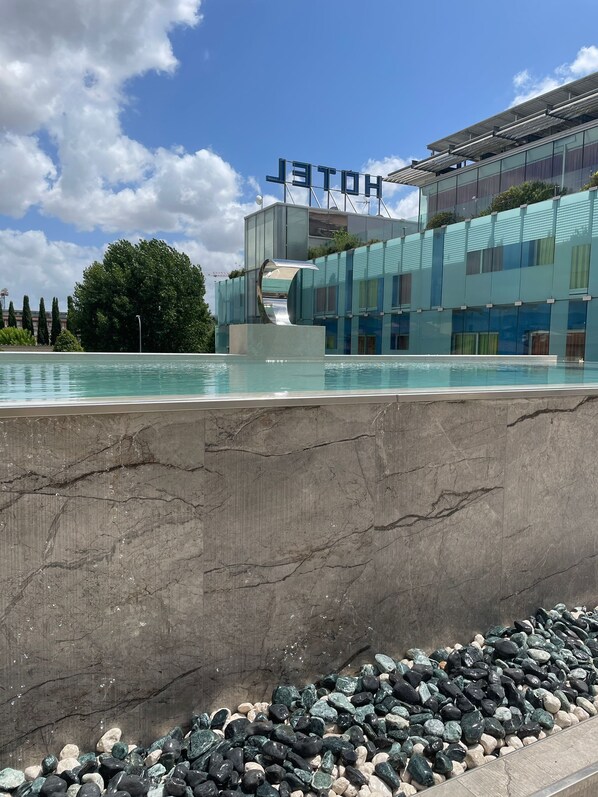 Un hotel moderno con fachada de vidrio, piscina y un letrero que dice "HOTEL".