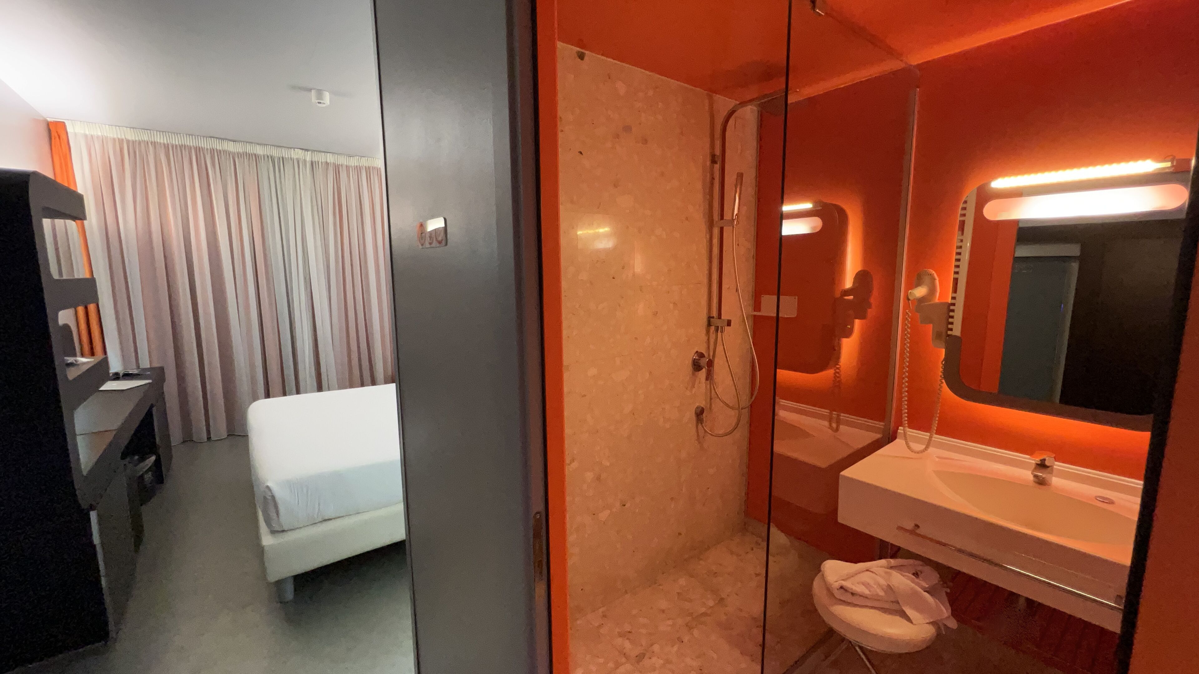A hotel room with a bed, a shower, and a bathroom with a mirror and sink.