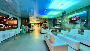 Un área de estar moderna con asientos, un bar y un restaurante al fondo.