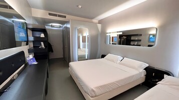 A hotel room with a bed, bedside tables, a desk with a computer, a mirror, and a door leading to a bathroom.