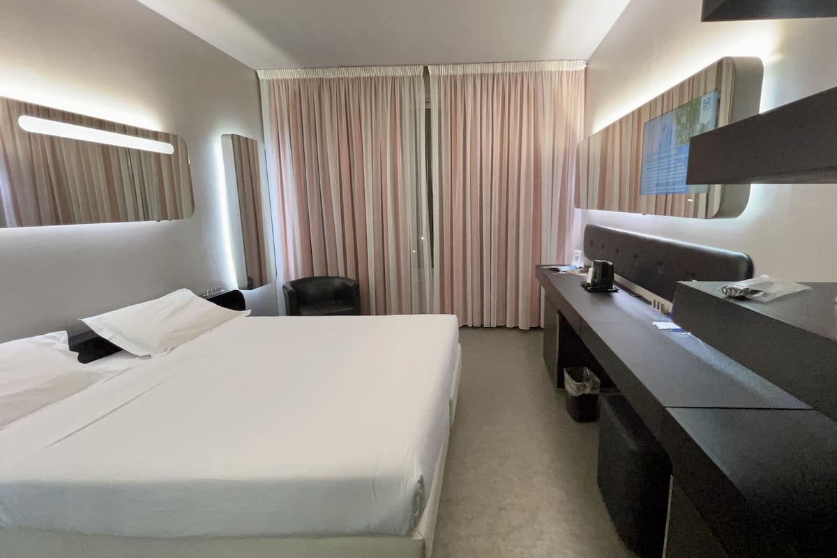 A hotel room with a bed, a desk, a chair, a TV, and a sign for Sky.