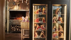 Una carnicería con una vitrina que exhibe diversos tipos de carne y un horno de leña al fondo.