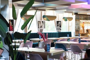 Un interior de restaurante moderno con mesas, sillas, una estantería y ventanas amplias.