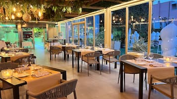 Un restaurante con varias mesas dispuestas para comer, ventanas amplias y plantas colgantes.
