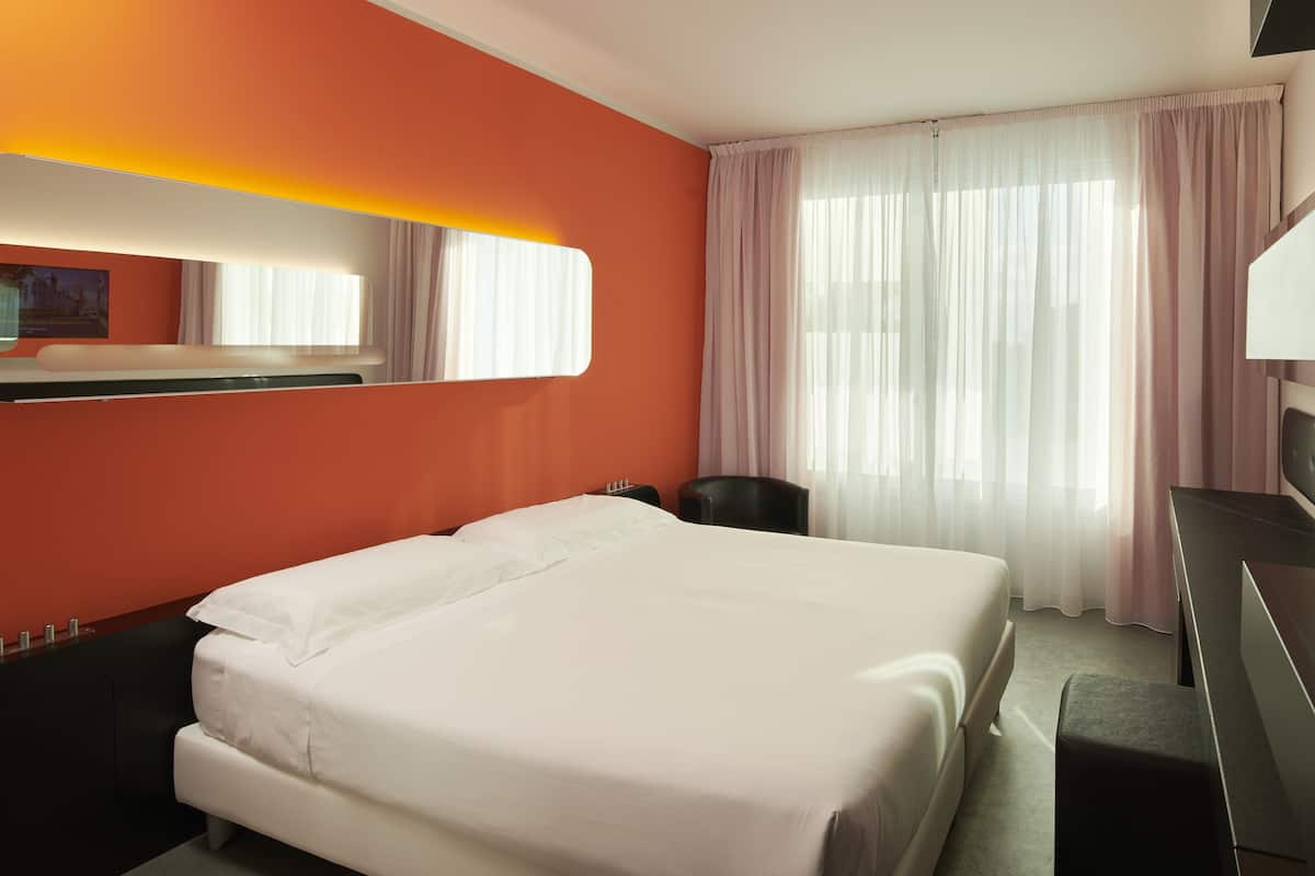 A hotel room with a large bed, a desk, and a chair.