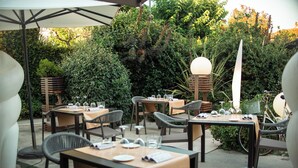 Un espacio de comedor al aire libre con mesas y sillas, rodeado de follaje y árboles.