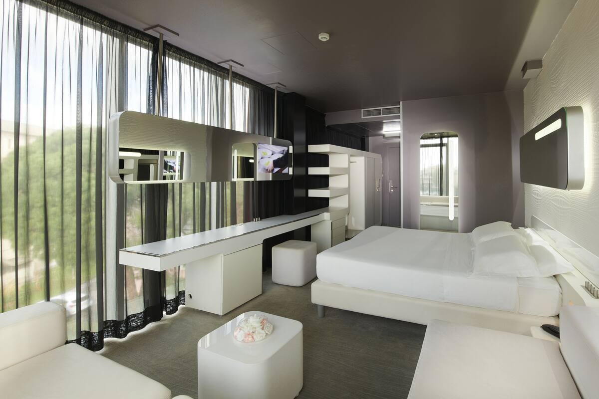 A modern hotel room with a large bed, a sofa, a desk, and a TV.