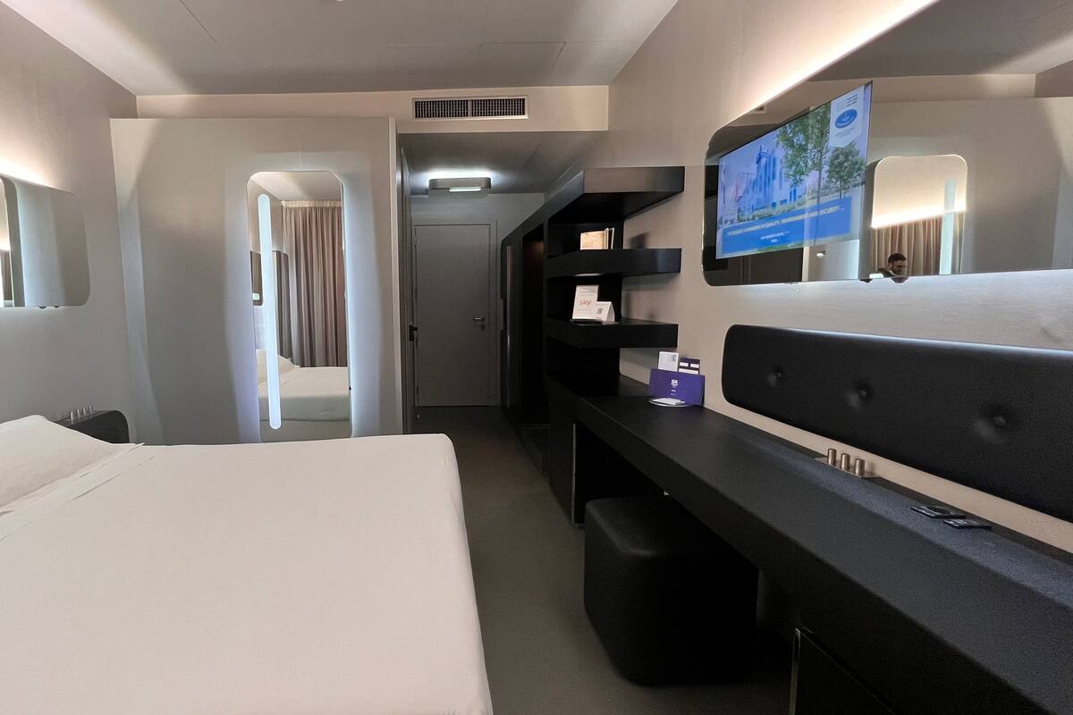 A hotel room with a large bed, a desk, a mirror, and a television.