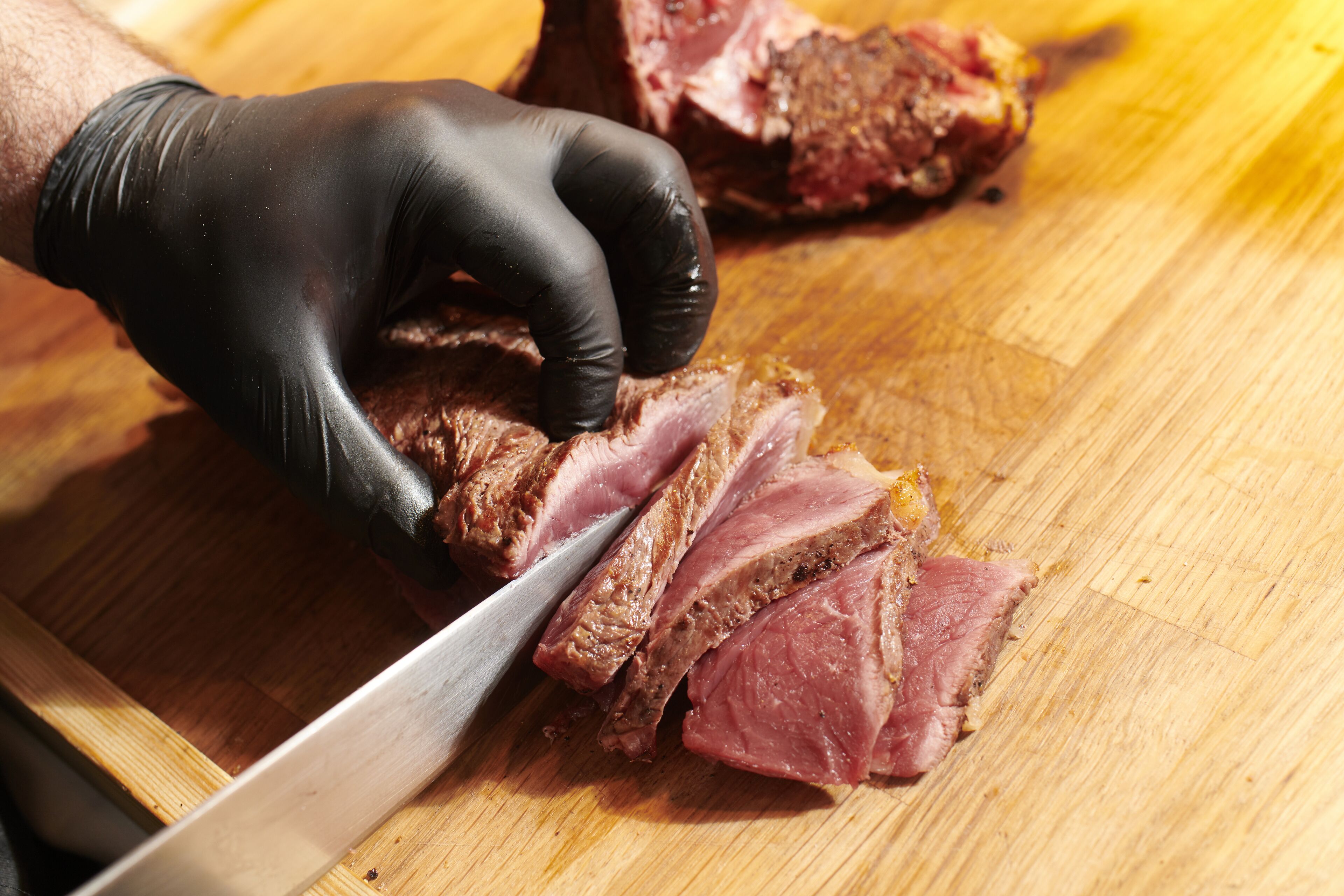 Une personne qui découpe un morceau de viande sur une planche à découper en bois.