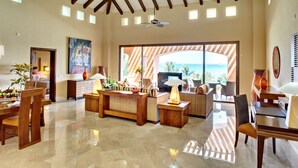 Un salón amplio con un ventanal que ofrece vistas al océano, un comedor con muebles de madera y una zona de estar acogedora con chimenea.