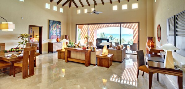 Un salón amplio con un ventanal que ofrece vistas al océano, un comedor con muebles de madera y una zona de estar acogedora con chimenea.