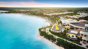 Vista aérea de un resort con playa, palmeras y un edificio grande con cúpula amarilla.