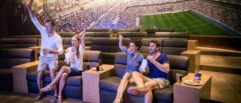 A movie theater with a large screen, reclining seats, and a stadium view mural.