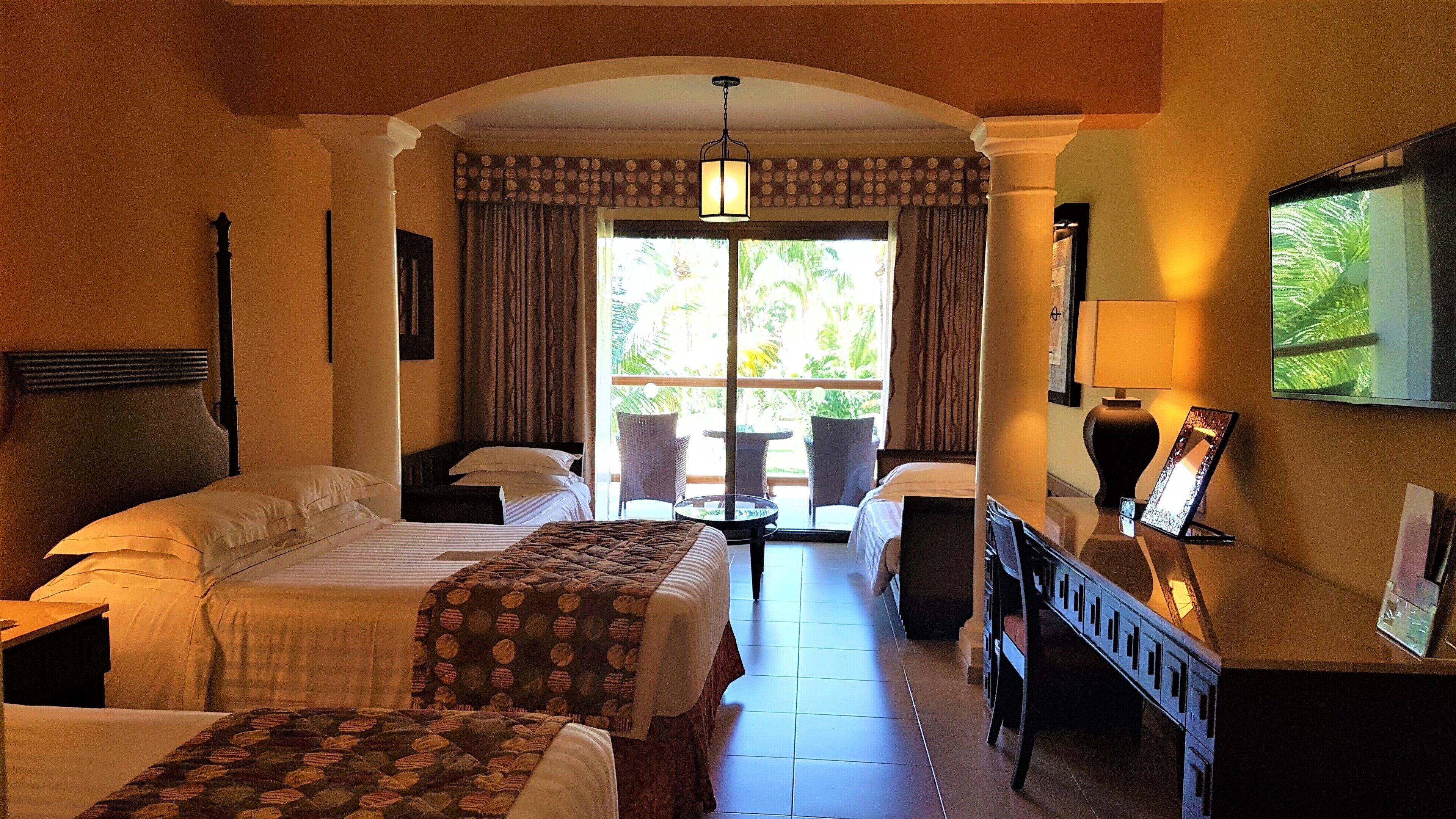 A hotel room with two beds, a desk with a chair, a TV, and a window with curtains.