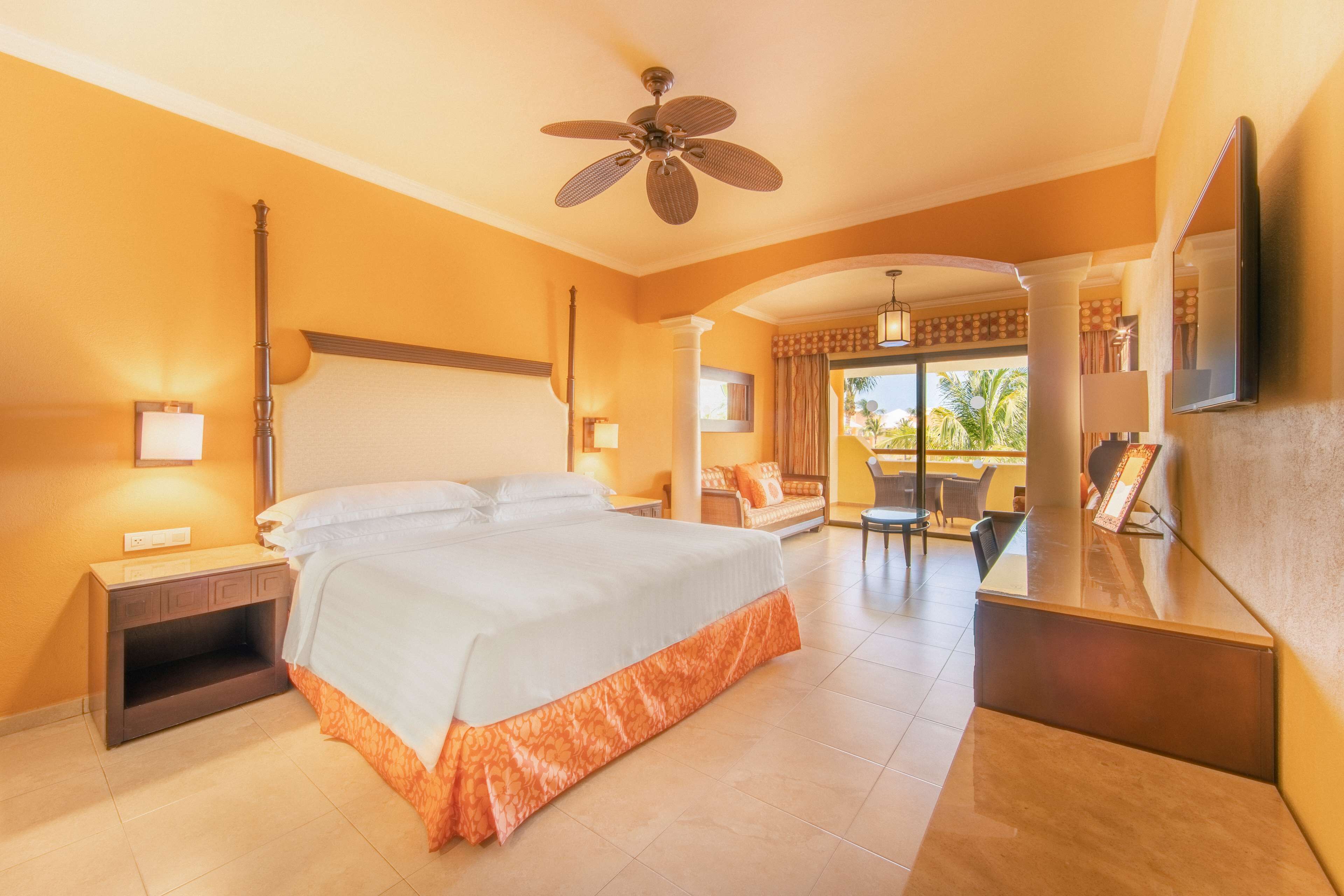 Quarto de hotel com uma cama grande, uma escrivaninha, um ventilador de teto e vista para o exterior.
