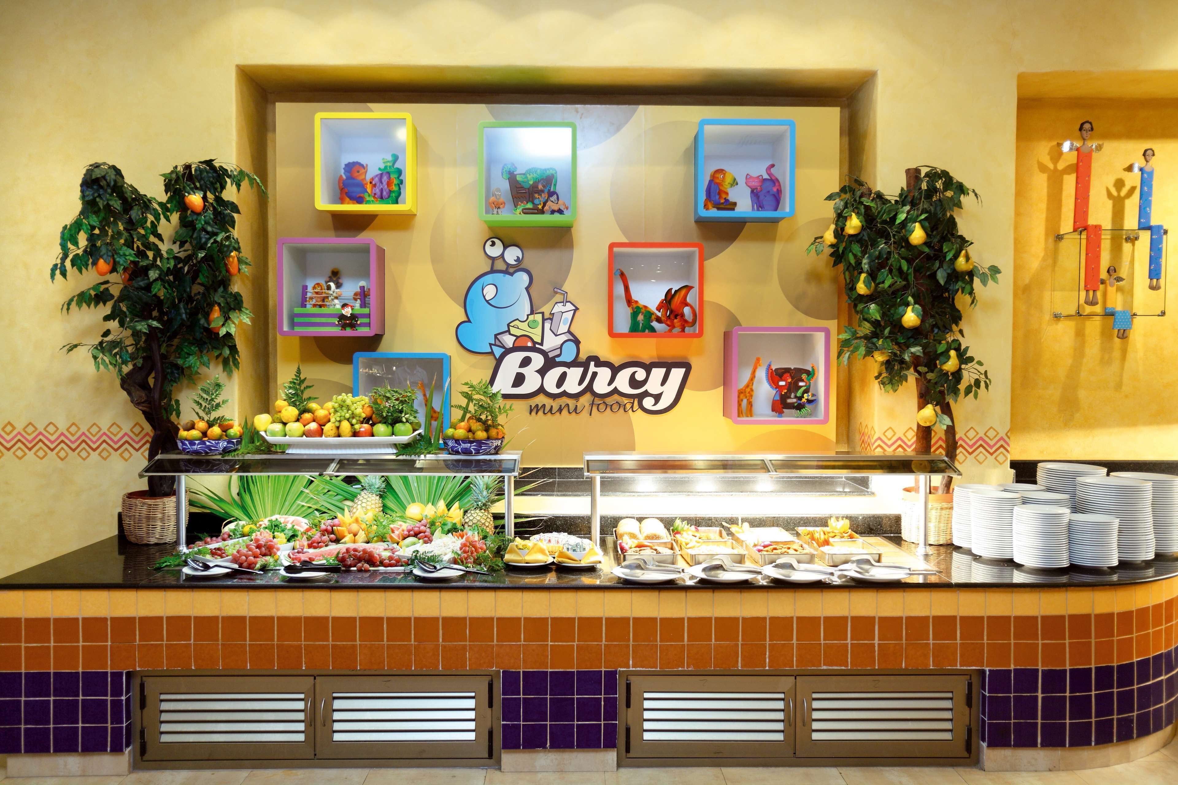 A buffet counter with a variety of food items, a sign reading "Barcy mini food," and colorful framed pictures on the wall.