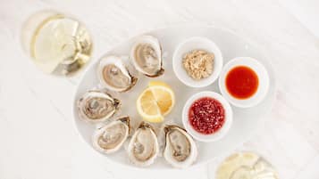 A plate of oysters with lemon wedges and two types of sauces.