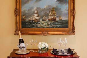 Una mesa servida con una botella de champán, copas, un florero y un cuadro enmarcado de barcos a vela.