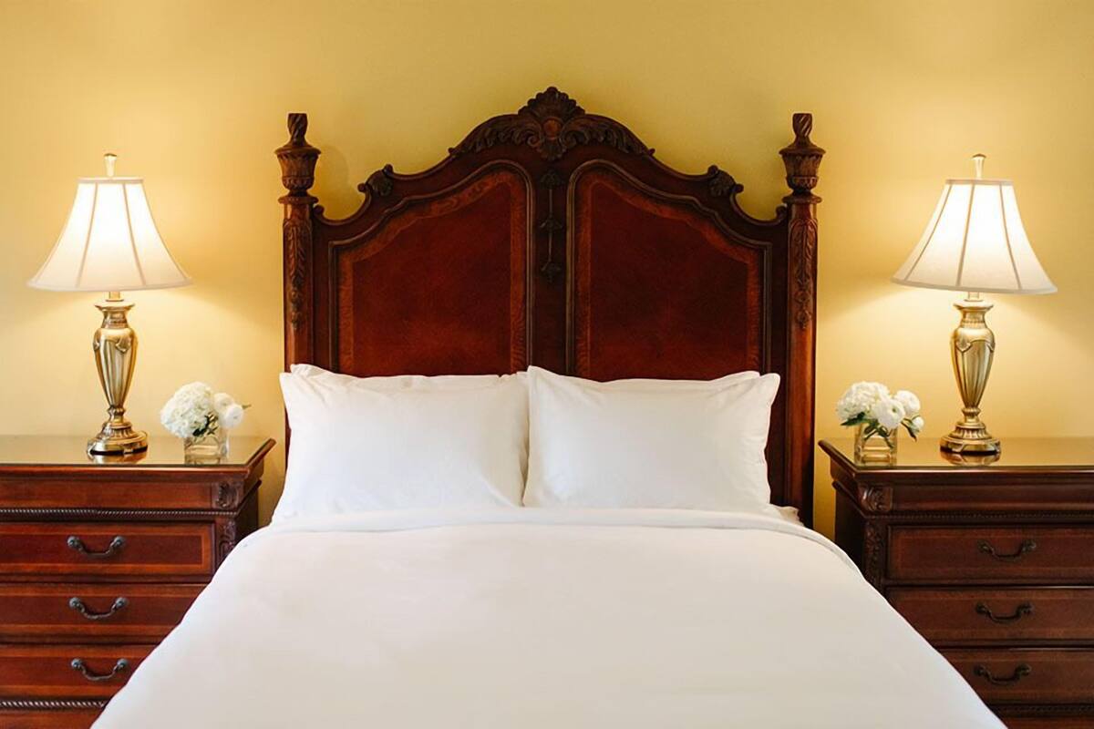 A neatly made bed with white linens, flanked by two bedside tables with lamps and small flower arrangements.