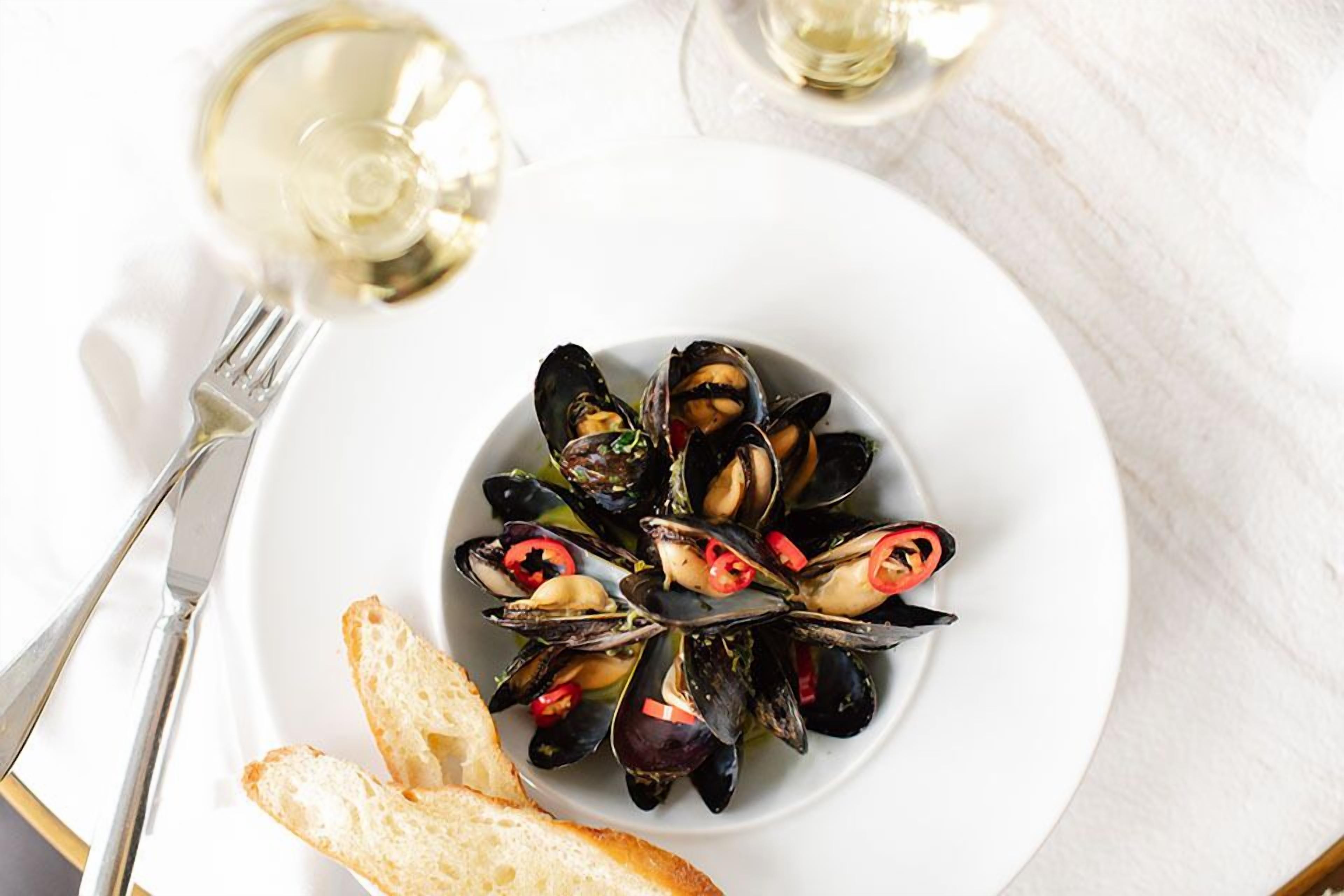 A plate of mussels with bread and a glass of white wine.