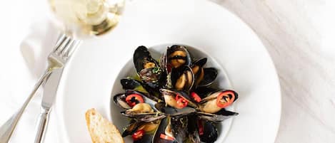 A plate of mussels with bread and a glass of white wine.