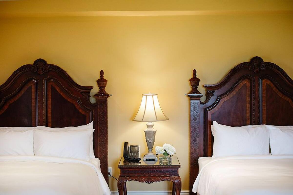 A hotel room with two wooden beds, a nightstand with a lamp, and a vase with flowers.