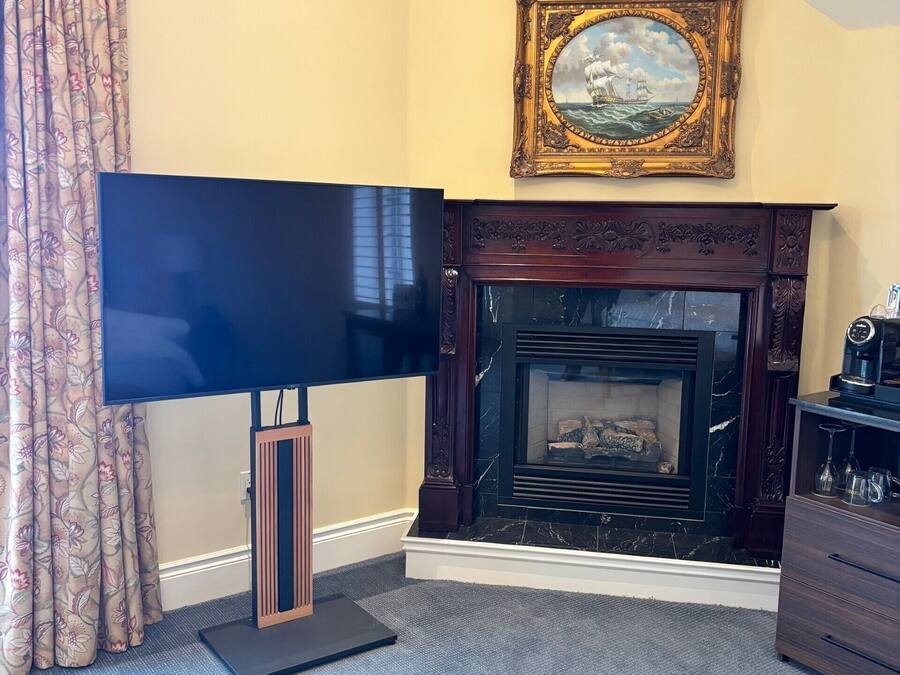 Una sala de estar con televisión de pantalla plana, chimenea, un cuadro enmarcado y cortina con estampado floral.