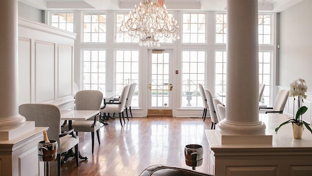 A spacious dining area with white chairs, a chandelier, and large windows.