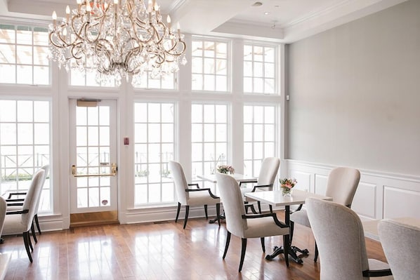 A dining area with a chandelier, large windows, and a white interior.