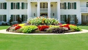 A large, white building with a sign reading "Riverbend Inn." It features a symmetrical facade with a central entrance flanked by columns, and a formal garden in front.