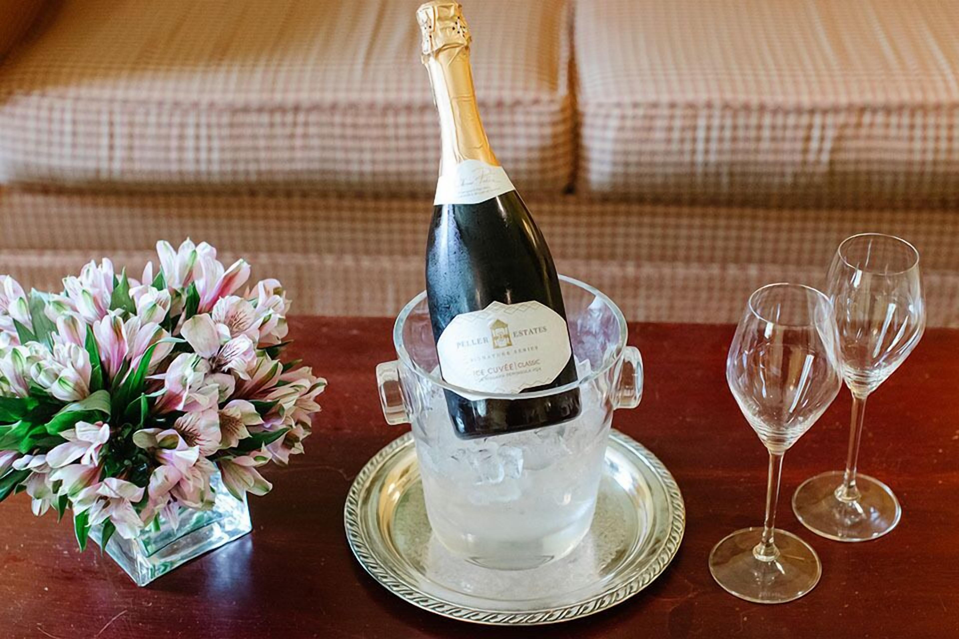 A bottle of champagne in an ice bucket on a tray, with two empty wine glasses beside it.