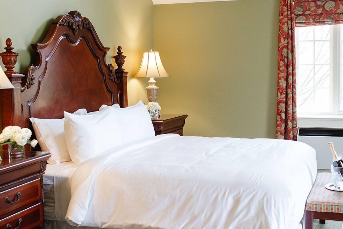 A neatly made bed with white linens, a wooden headboard, a bedside table with a lamp, and a vase of flowers.
