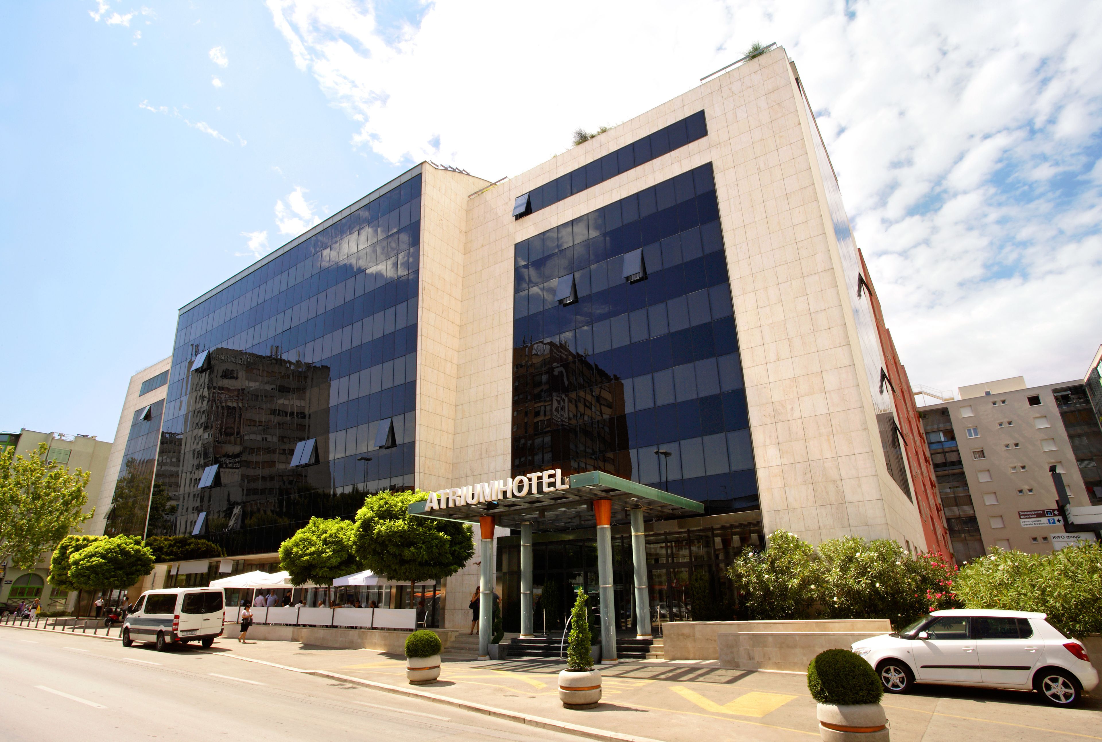 Un hotel moderno con fachada de vidrio, entrada cubierta y el letrero que dice "Atrium Hotel".