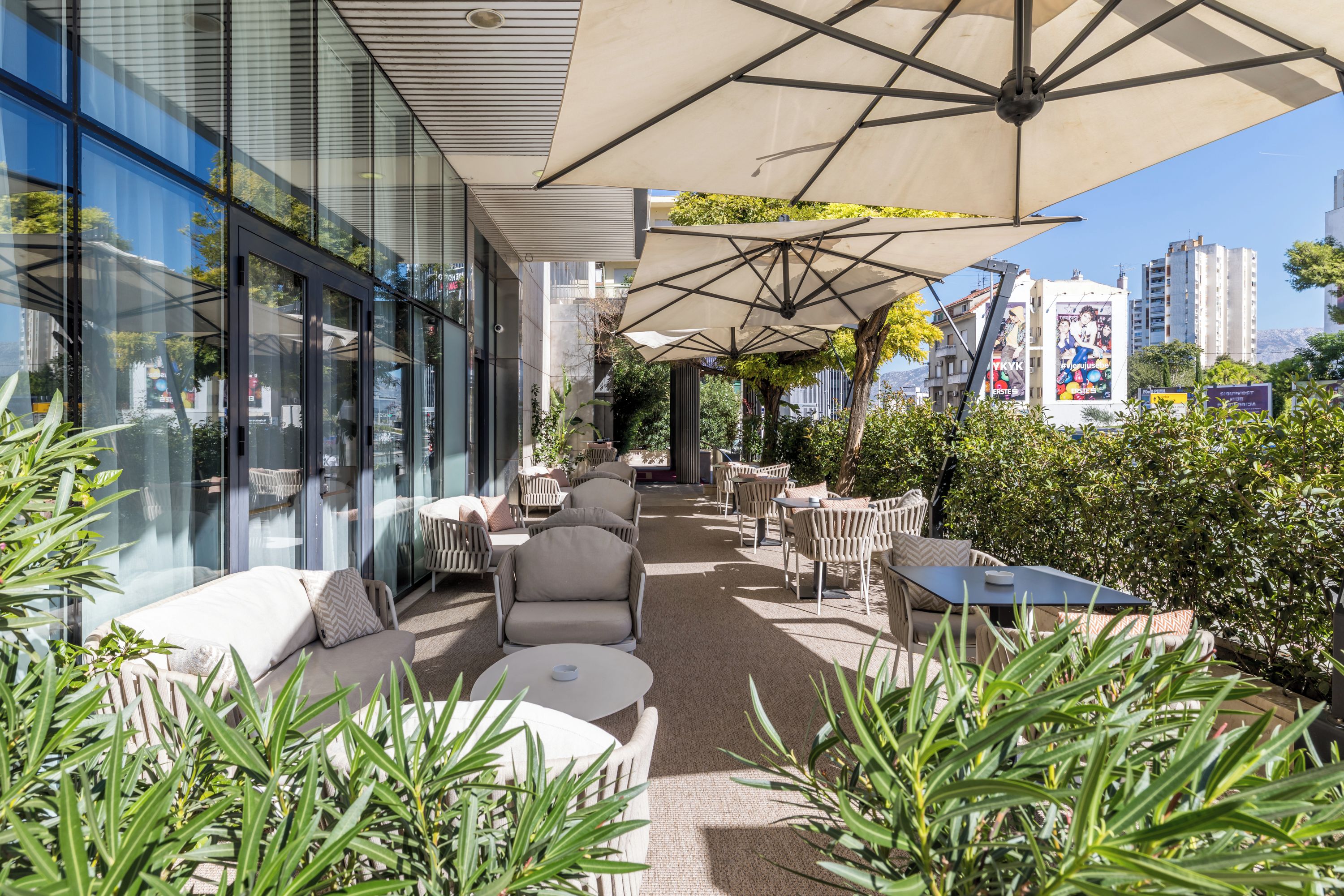 An outdoor seating area with tables and chairs, surrounded by greenery and a cityscape view.