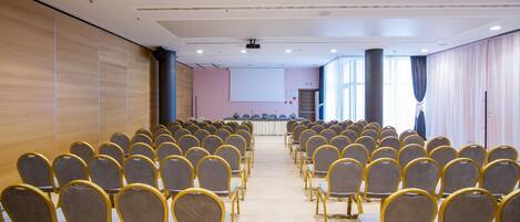Ein Konferenzraum mit Reihen von Stühlen, einer Projektionsleinwand und einer Bühne.
