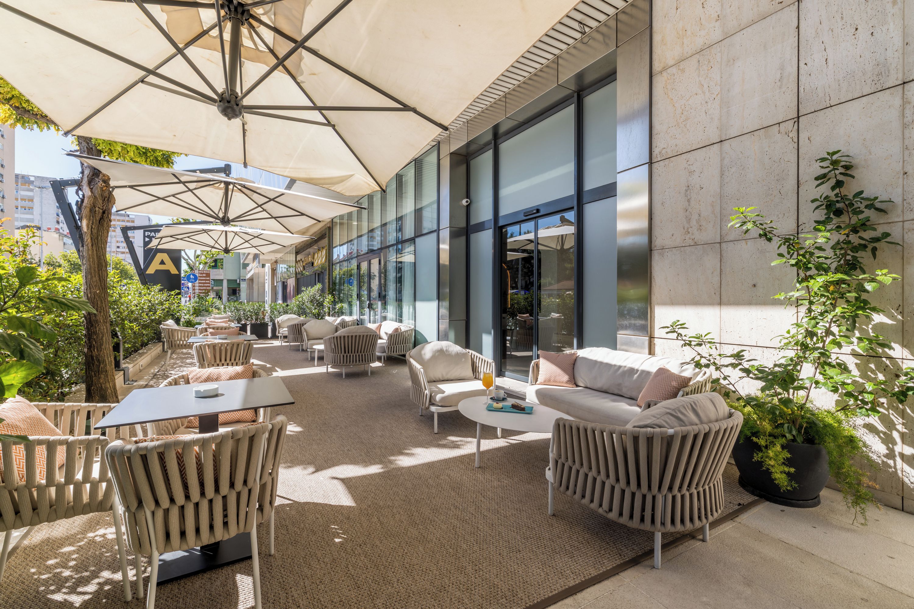 An outdoor seating area with wicker furniture, umbrellas, and a view of a building with large windows.