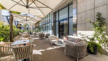 An outdoor seating area with wicker furniture, umbrellas, and a view of a building with large windows.